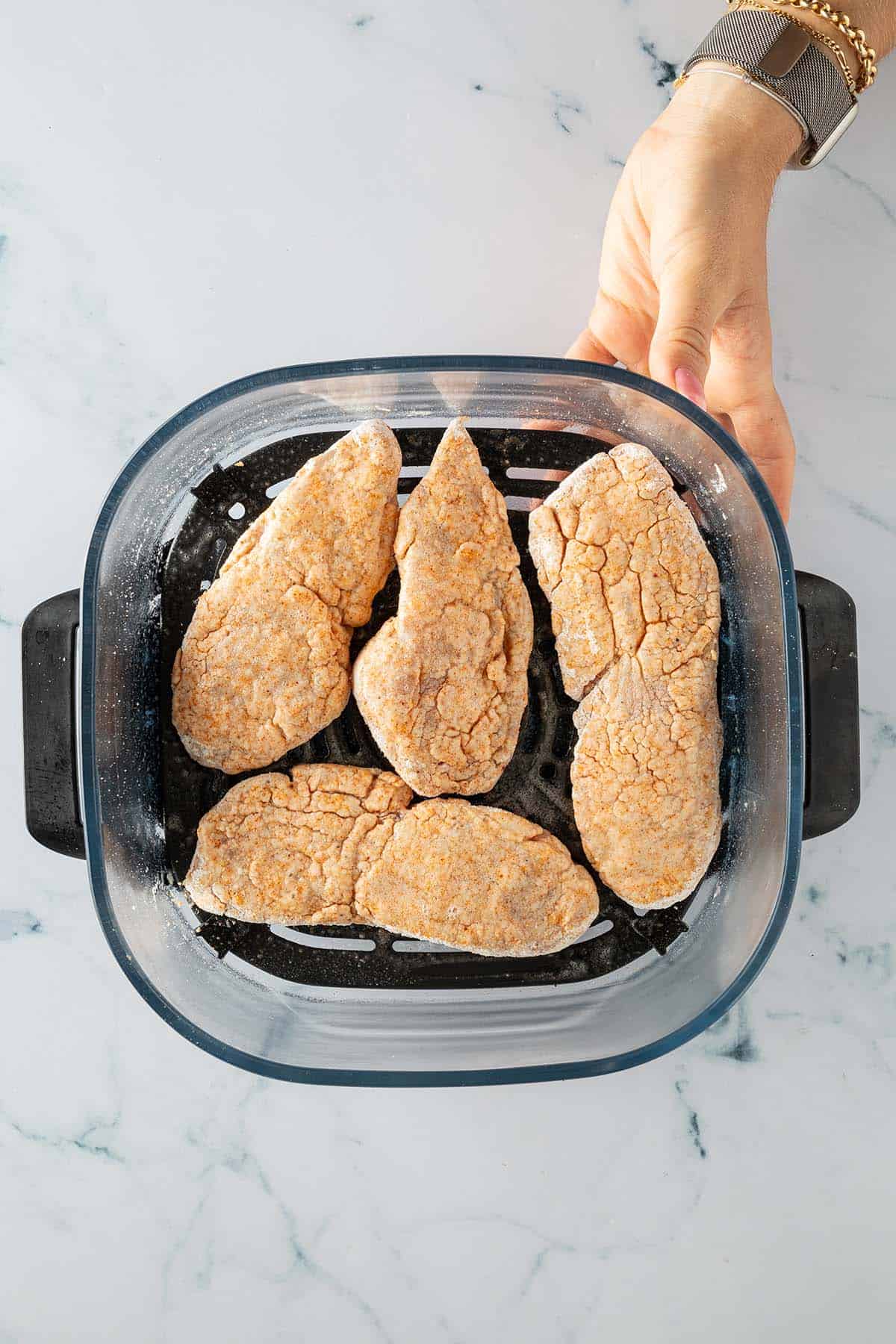 Panierte und eingeölte Hähnchenstücke vor dem Backen im Korb des Airfryers.