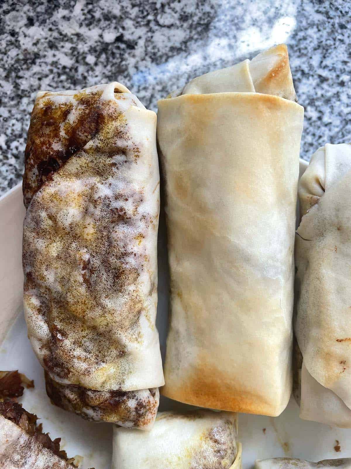 Zwei Frühlingsrollen auf einem Teller, eine davon in zwei Lagen Teig eingewickelt.