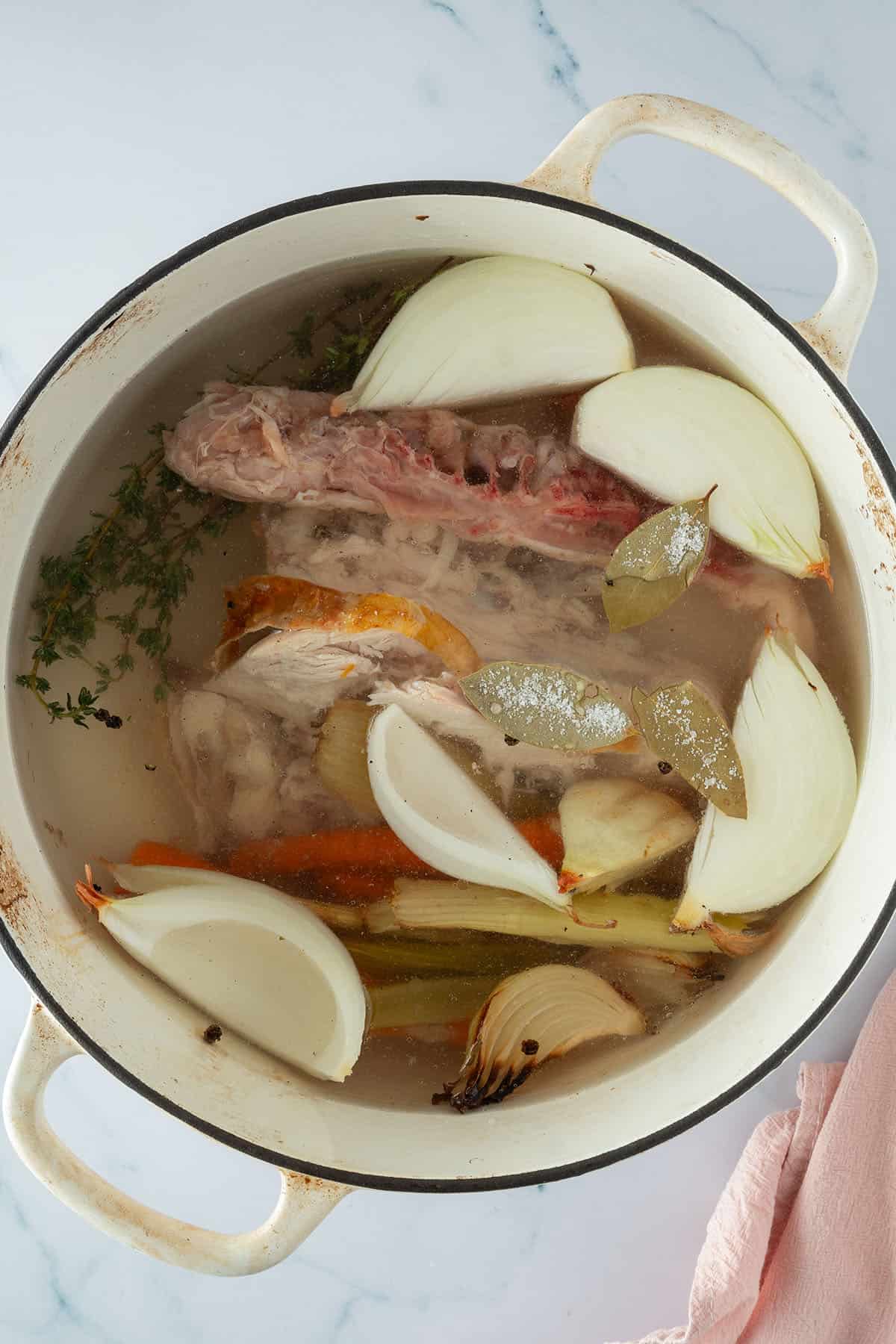 Hähnchenkarkasse, Zwiebeln, Karotten, Sellerie und Kräuter in einem großen Topf, angesetzt für eine selbstgemachte Hühnerbrühe.