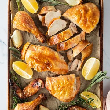 Ganzes Hähnchen aus dem Backofen aufgeschnitten auf einem Blech mit Zitronenspalten, Zwiebeln und frischen Kräutern.