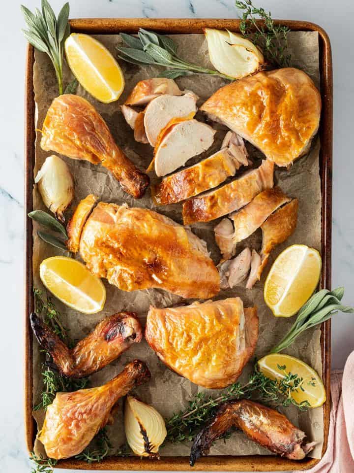 Ganzes Hähnchen aus dem Backofen aufgeschnitten auf einem Blech mit Zitronenspalten, Zwiebeln und frischen Kräutern.