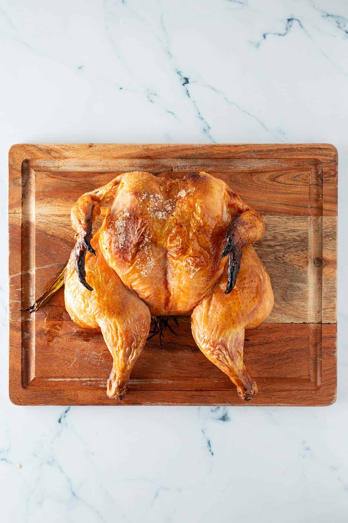 Ganzes, fertig gebratenes Hähnchen im Spatchcock-Stil auf einem Holzbrett.