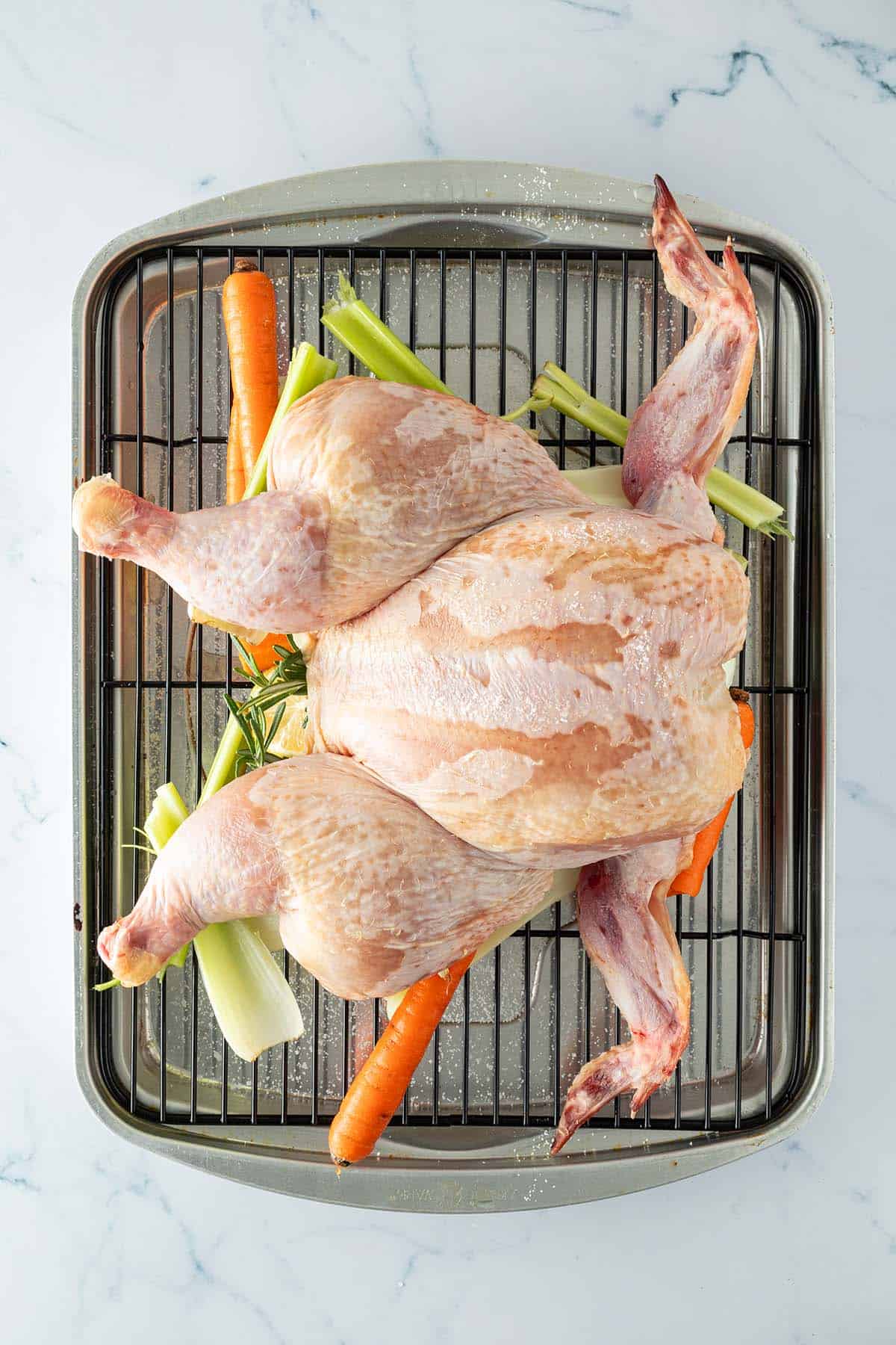 Roher, flach gedrückter Hähnchenkörper auf einem Rost über Gemüse.