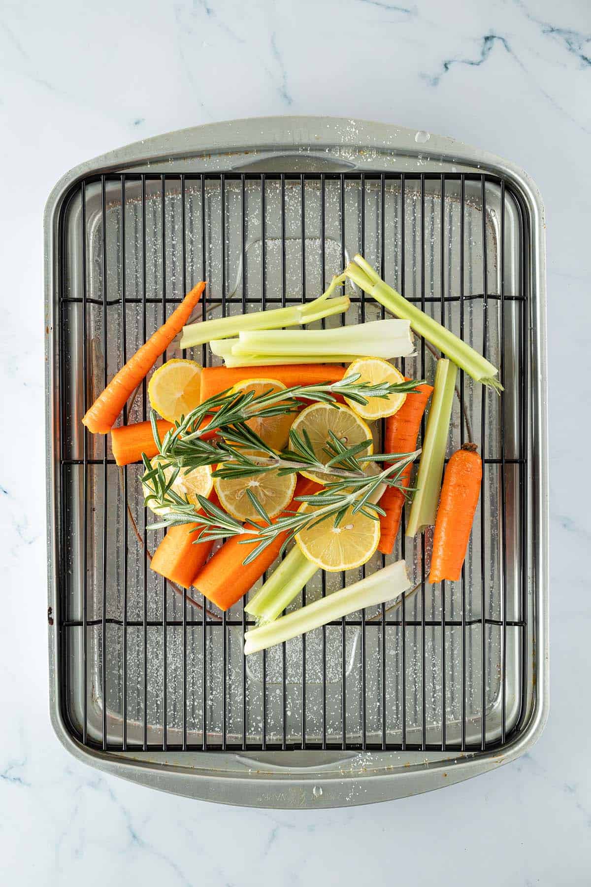Karotten, Sellerie, Zitronen und Rosmarin als Gemüsebett auf einem Backofenrost.