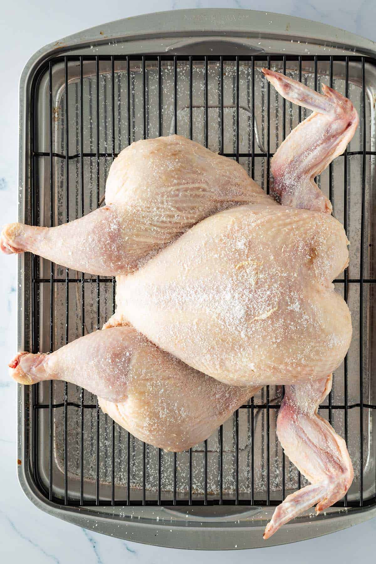 Roher Hähnchenkörper im Spatchcock-Stil, großzügig mit Salz bestreut auf einem Backofenrost.