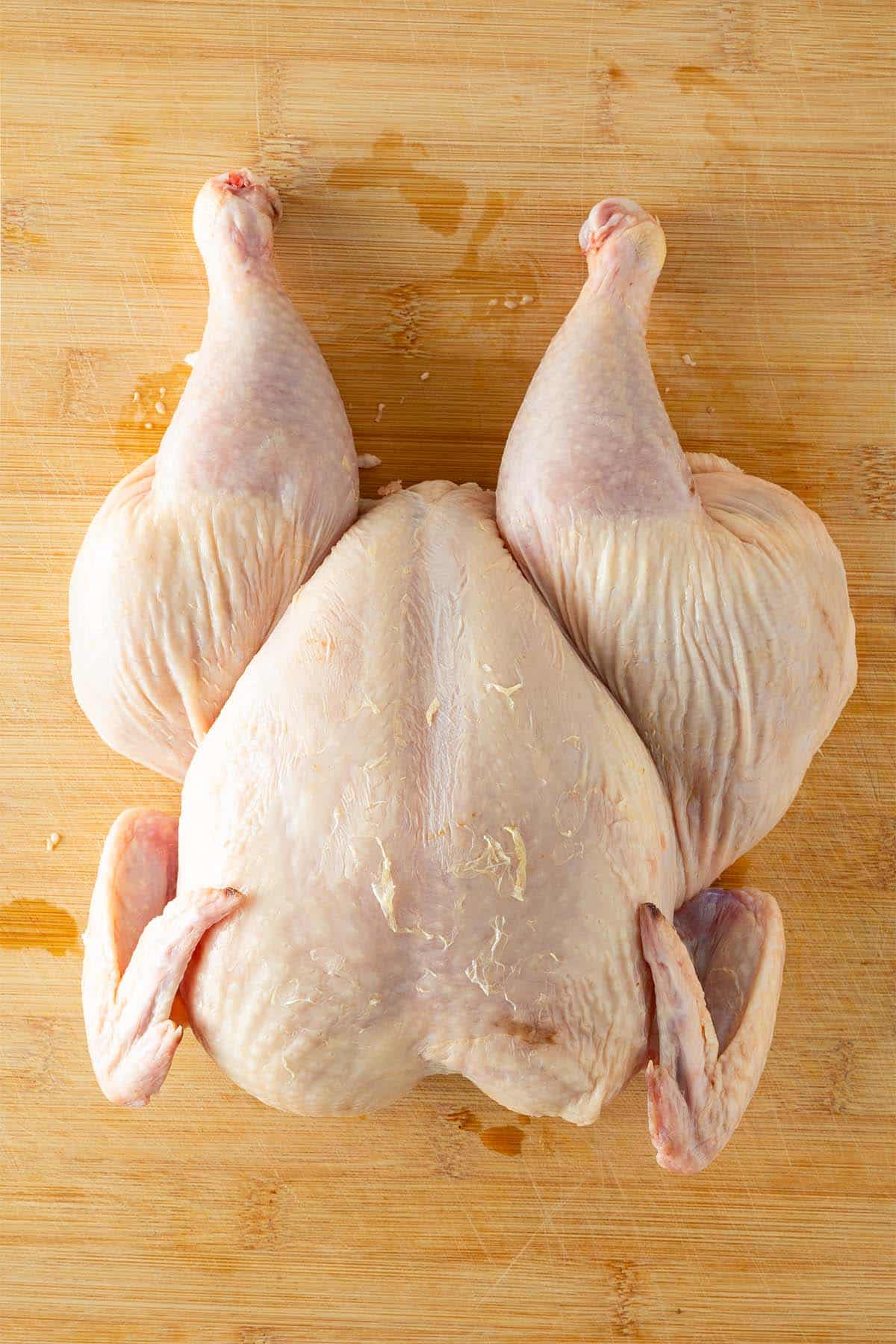 Ganzes, rohes Hähnchen auf einem Holzbrett mit entferntem Rückgrat.
