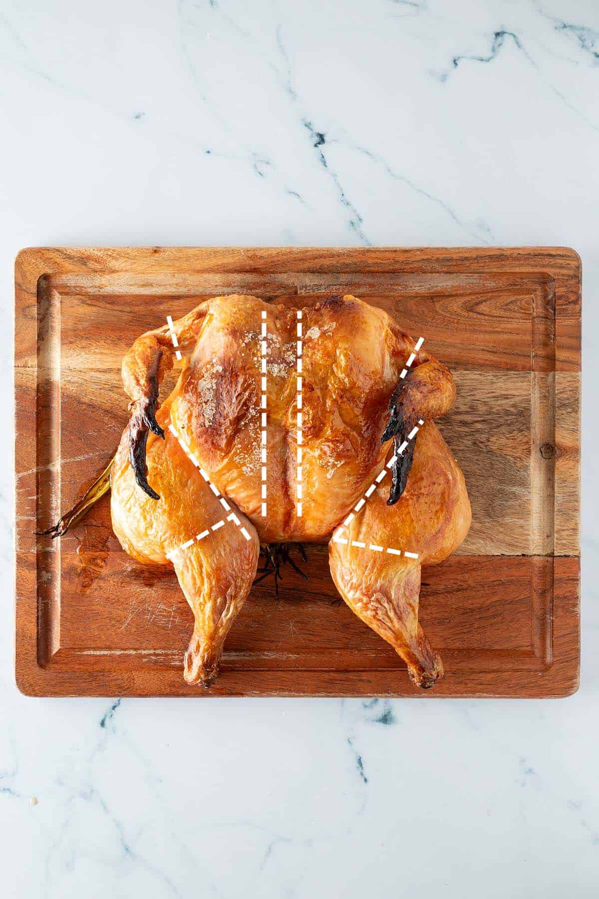 Ganzes, gebratenes Hähnchen im Spatchcock-Stil auf einem Holzbrett, mit eingezeichneten Schnittlinien zum Zerlegen.