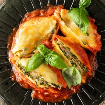 Mit Spinat Ricotta und Thunfisch gefüllte Muschelnudeln auf einem Teller mit Tomatensauce und frischem Basilikum.