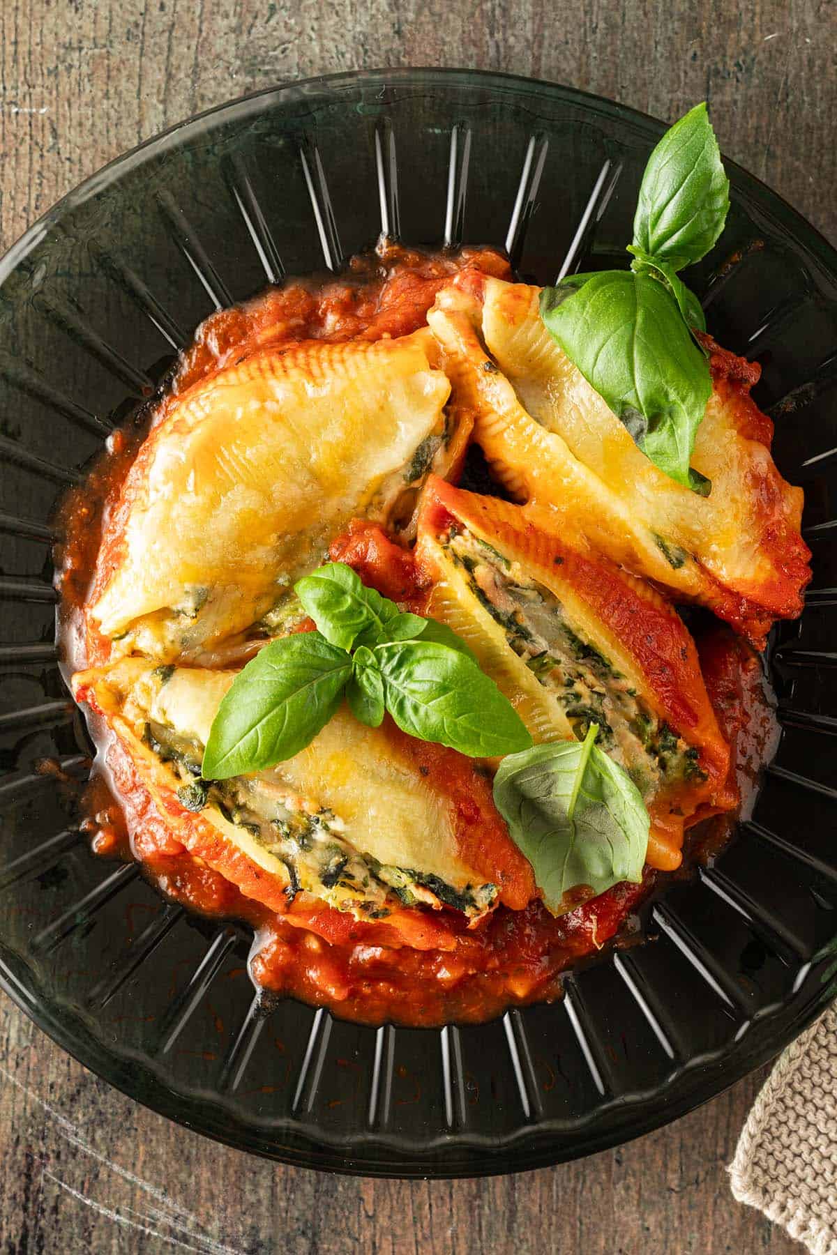 Mit Spinat Ricotta und Thunfisch gefüllte Muschelnudeln auf einem Teller mit Tomatensauce und frischem Basilikum.