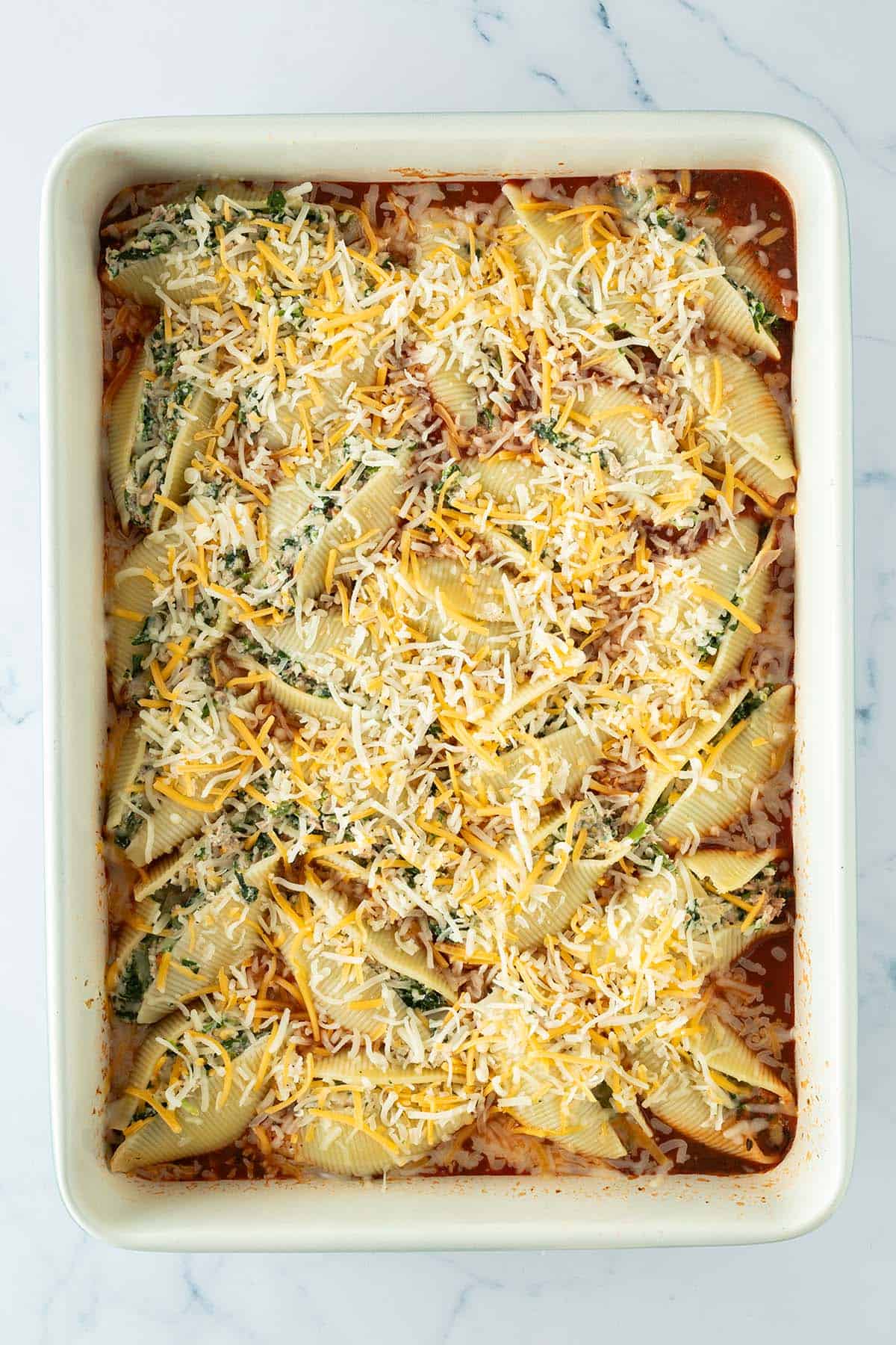 Käse wurde über mit einer Spinatfüllung gefüllte Muschelnudeln in einer Auflaufform mit Tomatensauce gestreut.