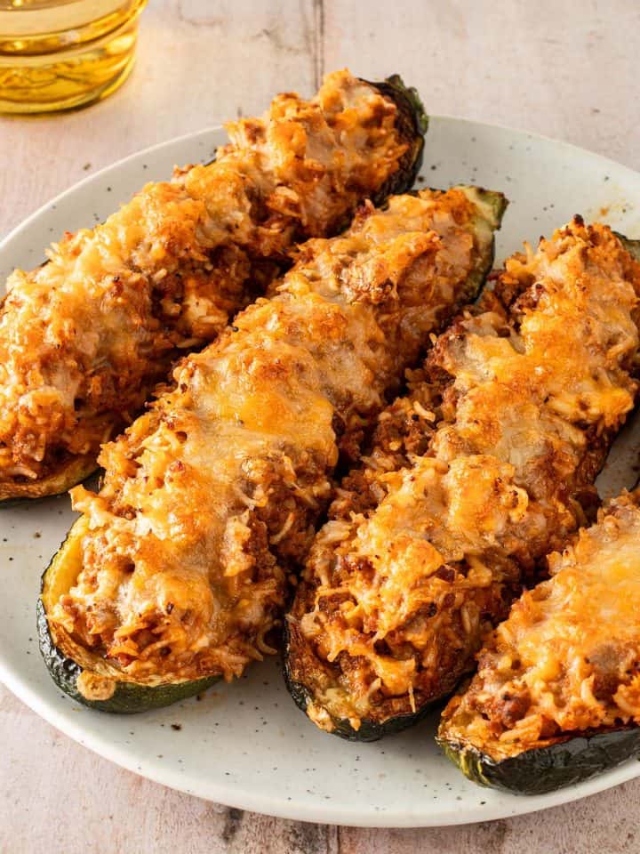 Überbackene, gefüllte Zucchinihälften mit Reis, Hackfleisch und geschmolzenem Käse auf einem Teller serviert.