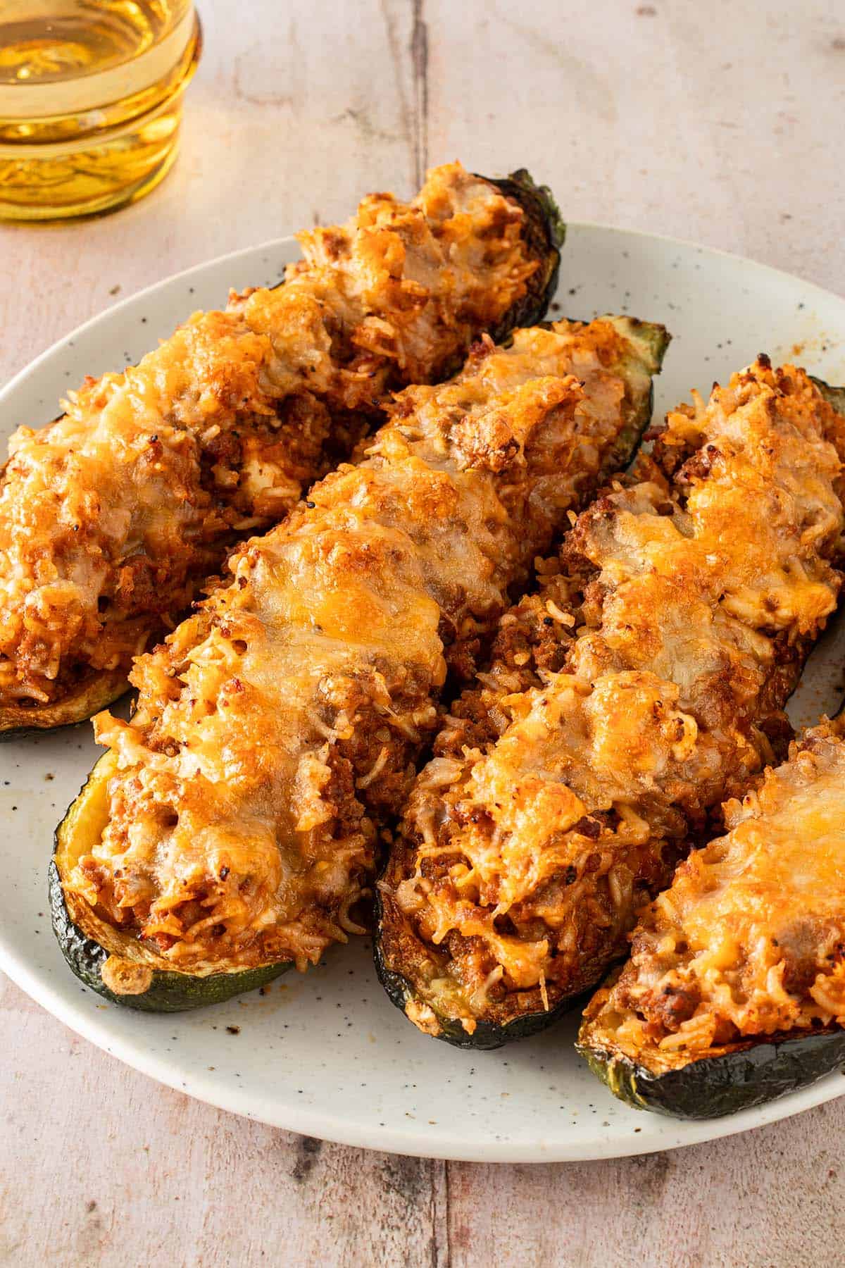 Überbackene, gefüllte Zucchinihälften mit Reis, Hackfleisch und geschmolzenem Käse auf einem Teller serviert.