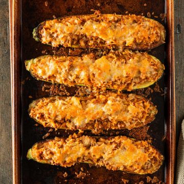 Vier gefüllte Zucchinihälften mit goldbrauner Käsekruste auf einem Backblech aus dem Ofen.