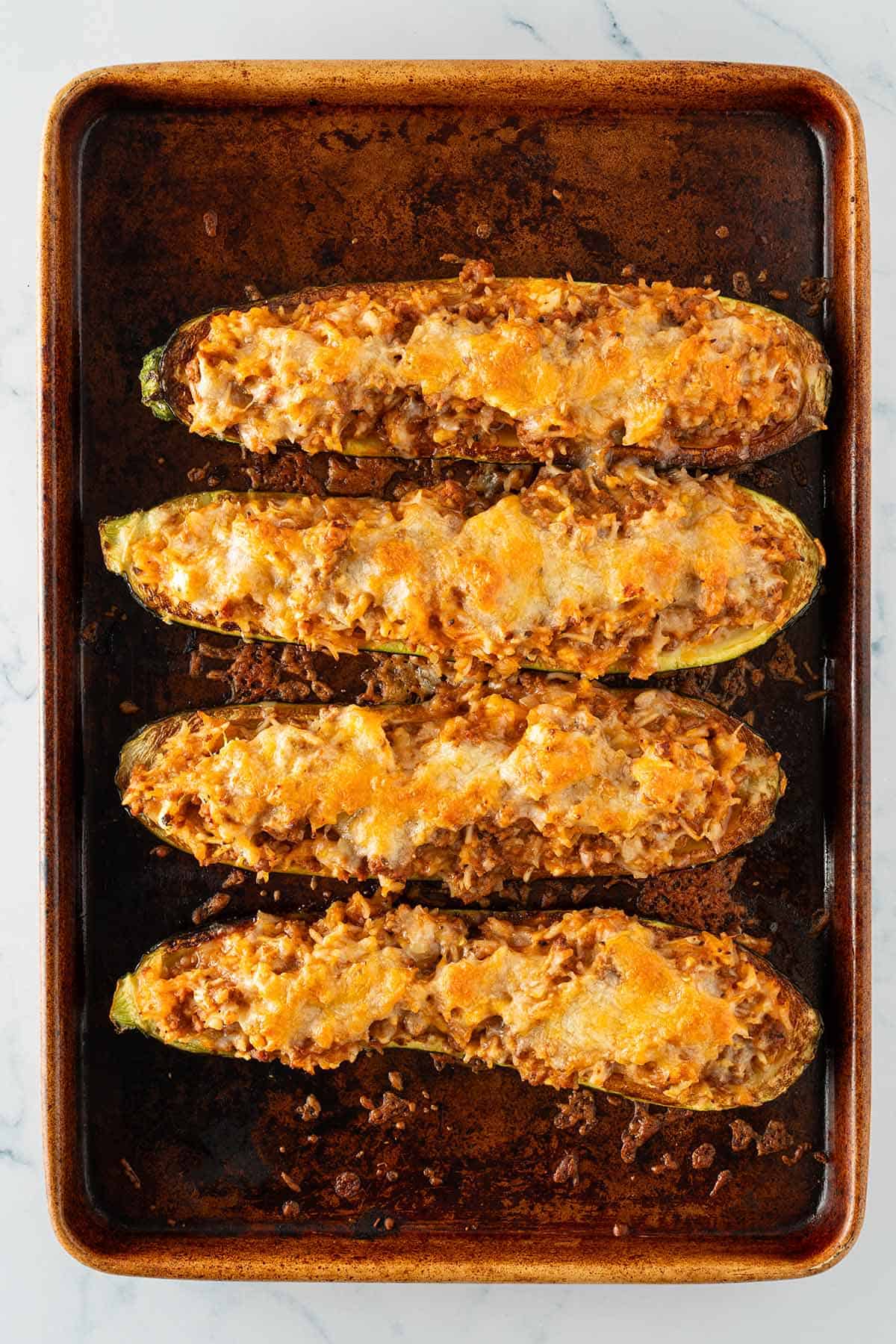 Gefüllte Zucchinihälften mit geschmolzenem Käse auf einem Backblech.