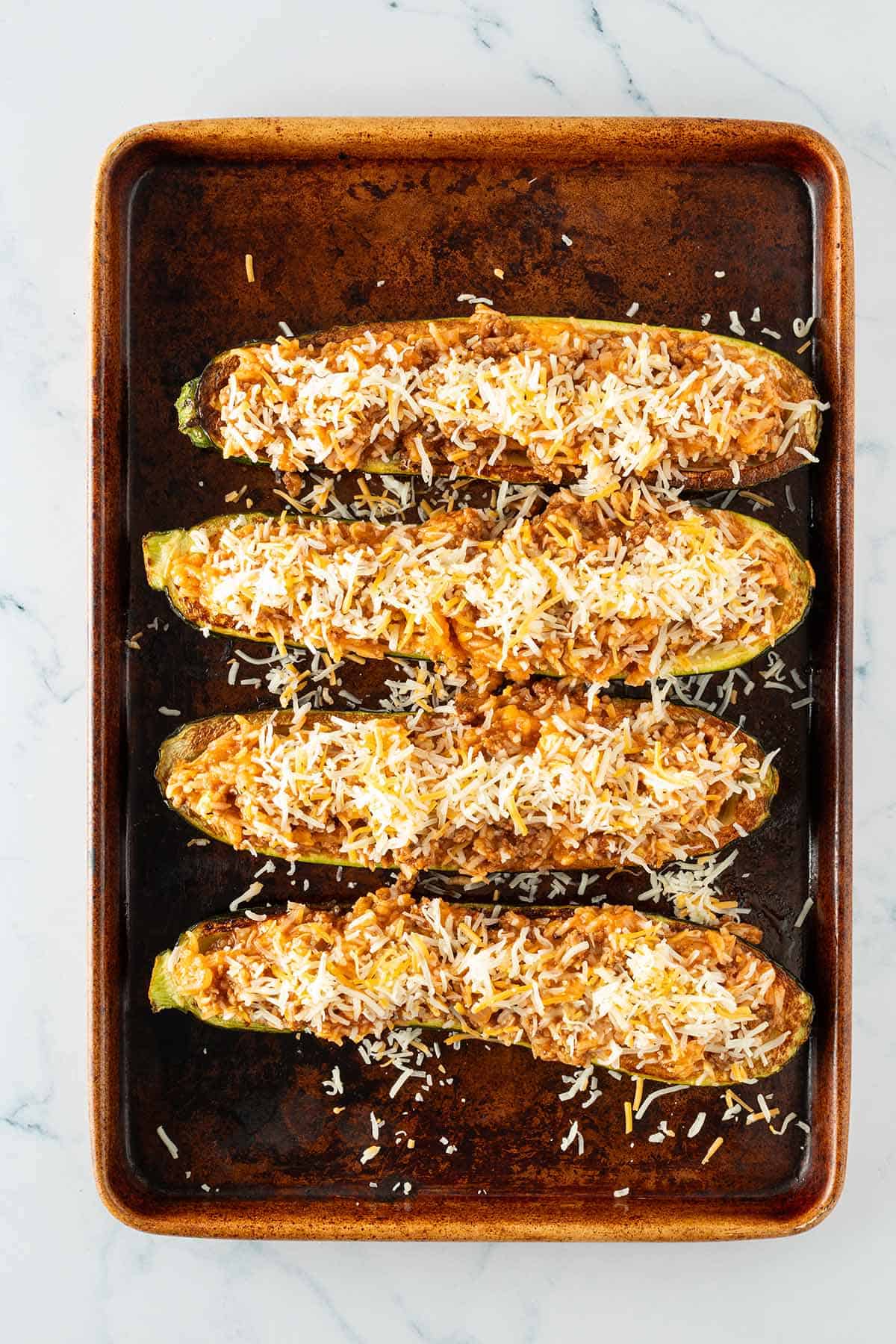 Rohe gefüllte Zucchinihälften mit der Reis-Pfanne gefüllte und geriebenem Käse vor dem Backen auf einem Blech.