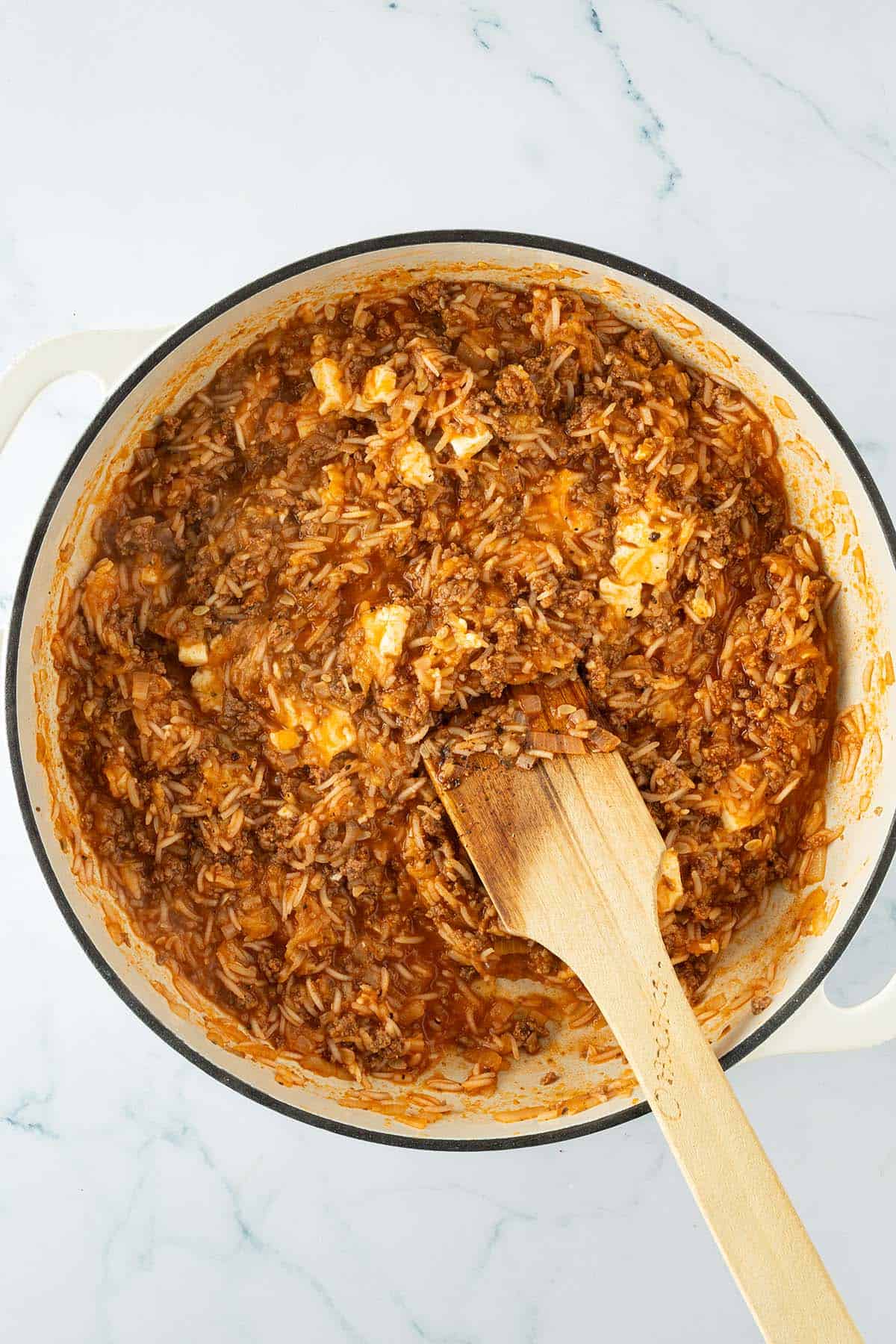 Reis-Hackfleisch-Füllung mit Tomatensoße und Feta in einer Pfanne, mit Holzlöffel gerührt.