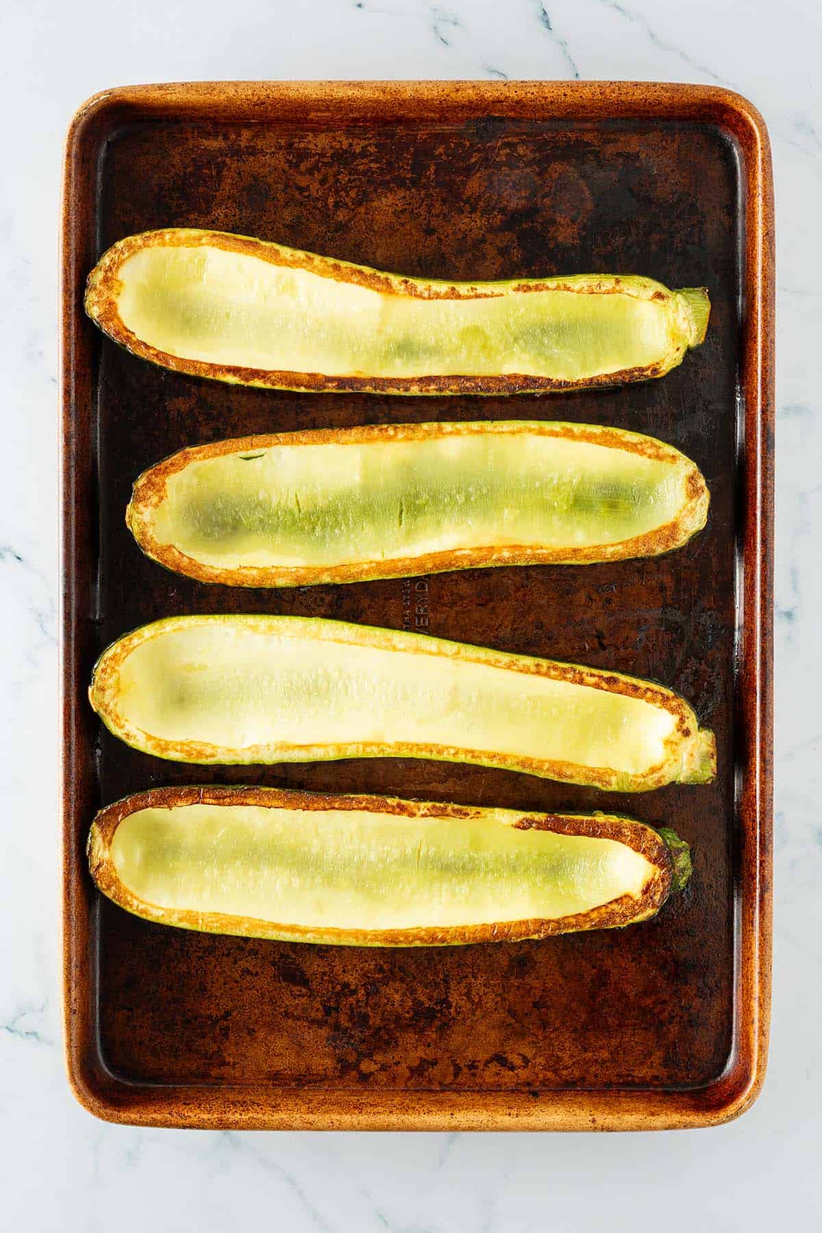 Ausgehöhlte und im Ofen geröstete Zucchinihälften auf einem Backblech, bereit zum Füllen.
