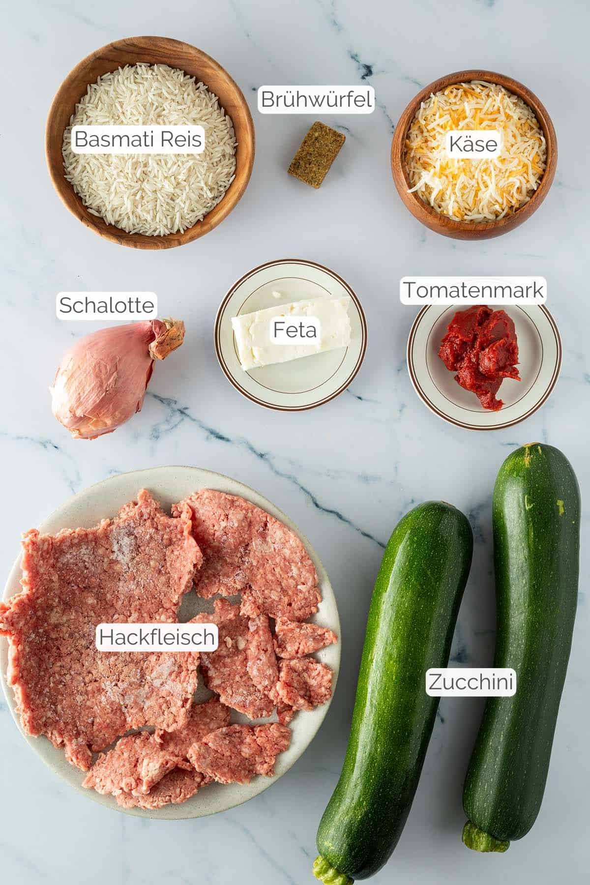 Alle Zutaten mit jeweiligen Textbeschriftungen, die für die gefüllten Zucchini mit Reis benötigt werden.