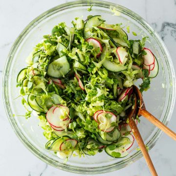 Gemischter Beilagensalat mit Gurken, Salat, Radieschen in einer großen Glasschüssel mit Salatbesteck.
