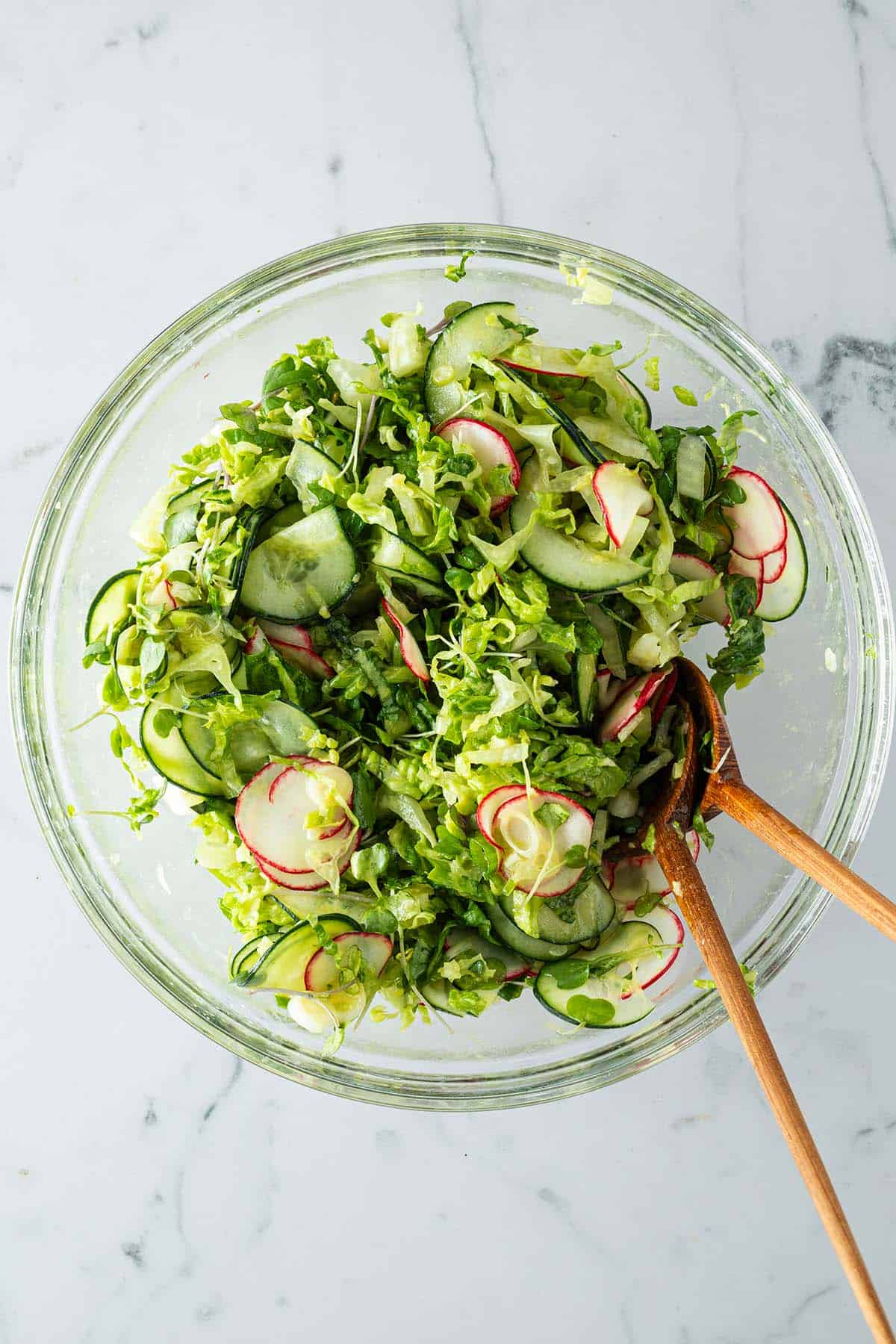 Gemischter Beilagensalat mit Gurken, Salat, Radieschen in einer großen Glasschüssel mit Salatbesteck.