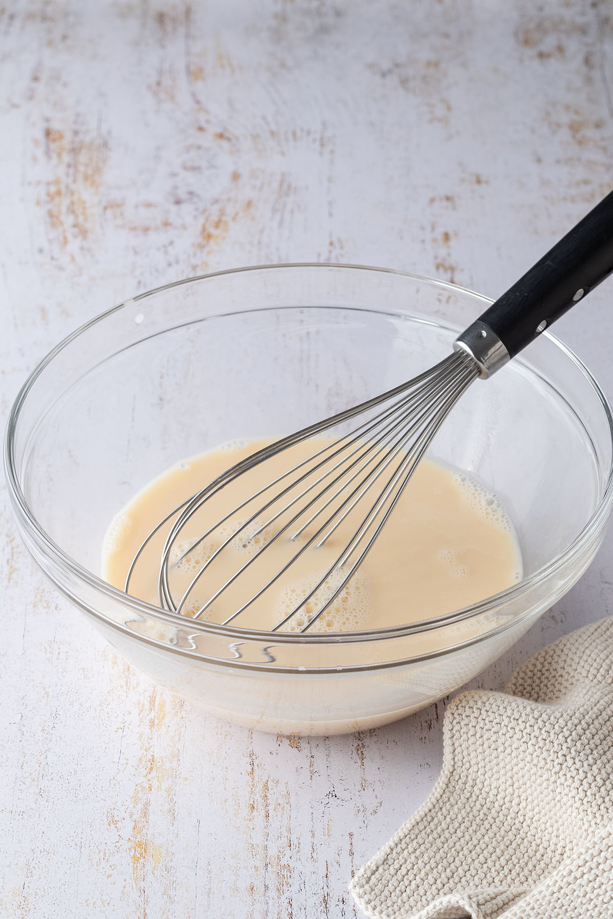 Eine Glassch&uuml;ssel mit einer Eier-Milch-Mischung, die mit einem Schneebesen verr&uuml;hrt wurde.
