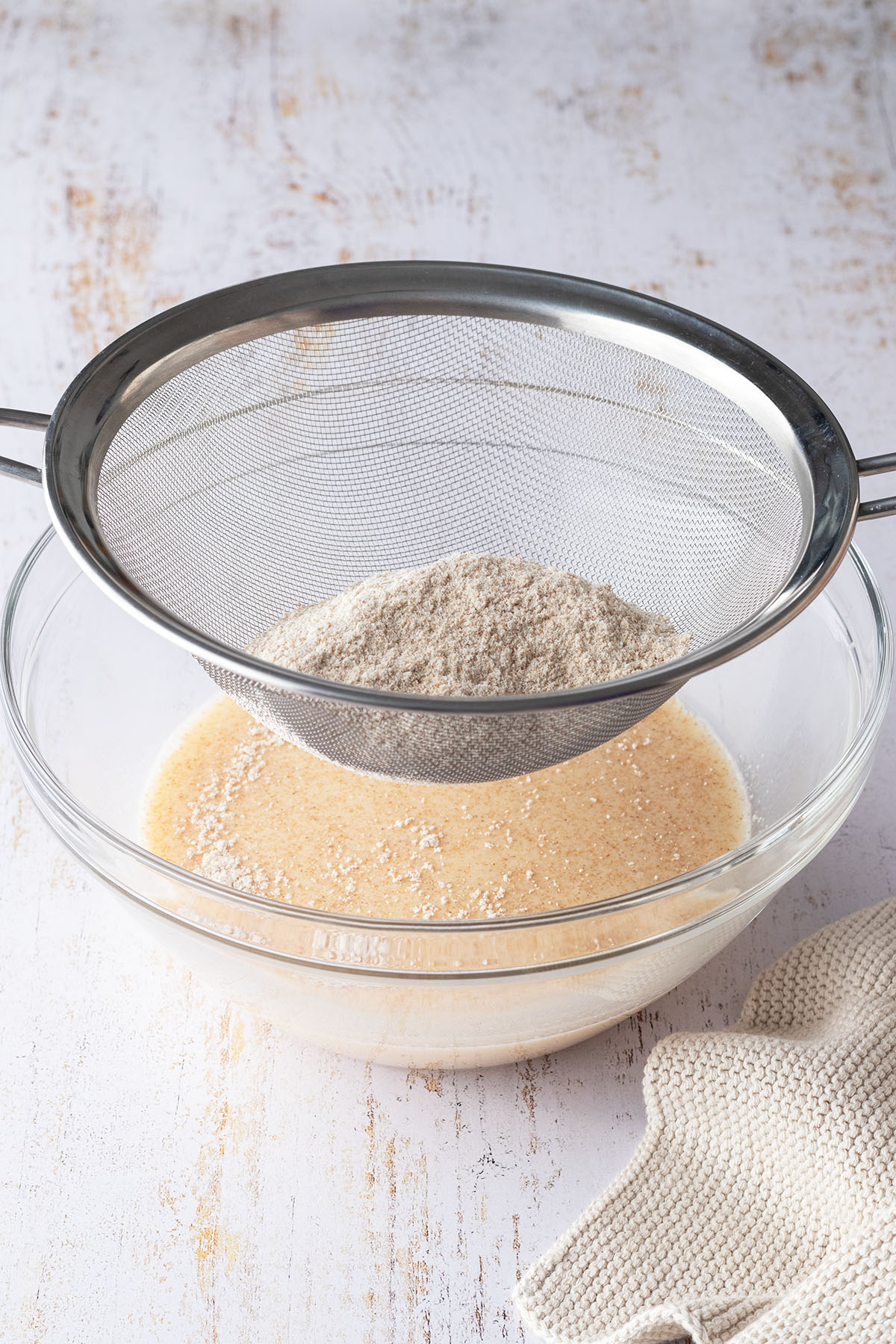 Mit einem feinen Sieb wird Vollkornmehl in eine Glassch&uuml;ssel mi einer Eier-Milch-Mischung gesiebt.