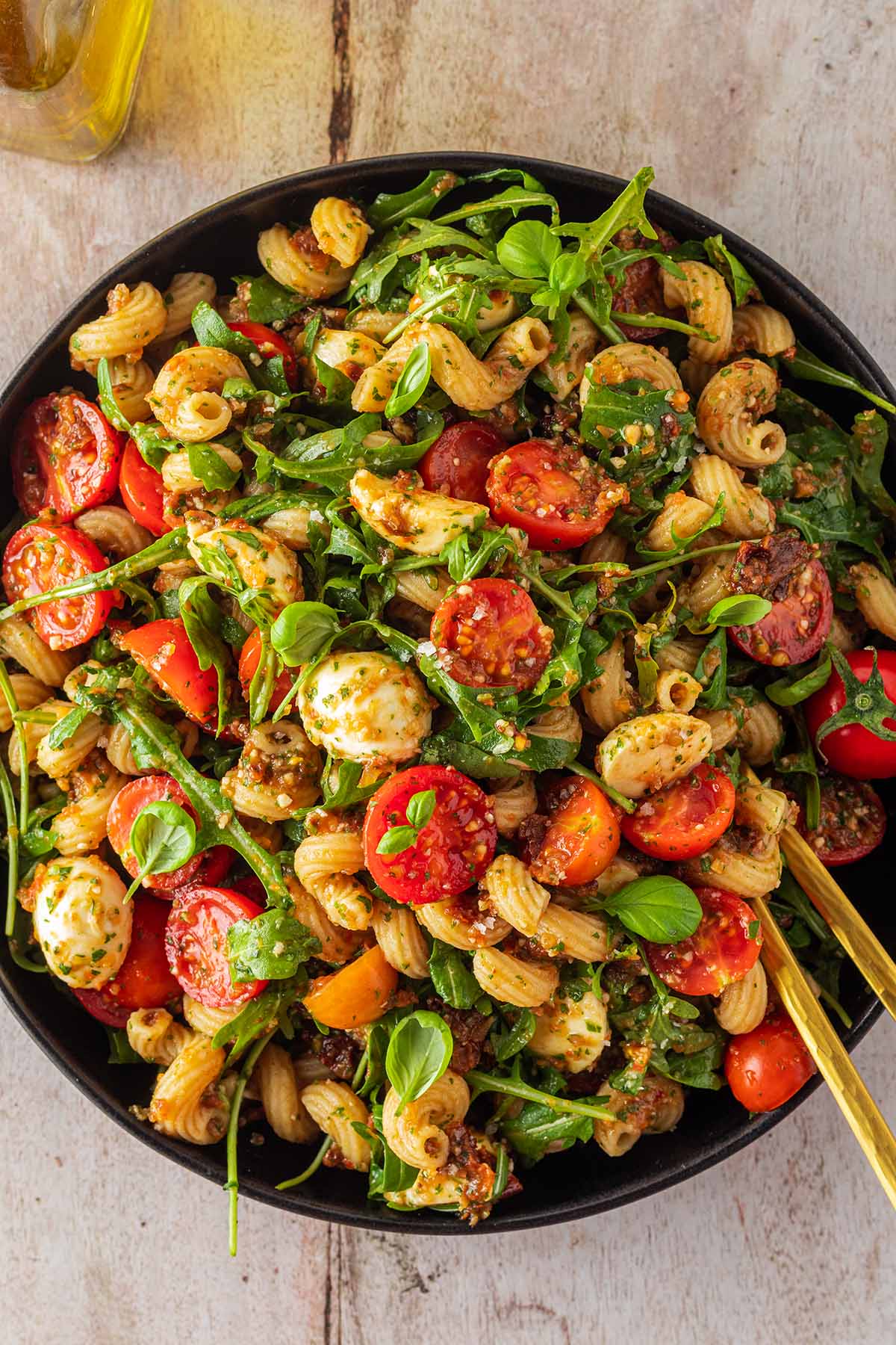 Große Portion Nudelsalat mit Tomaten, Rucola, Mozzarella und Pesto in einem tiefen Teller.