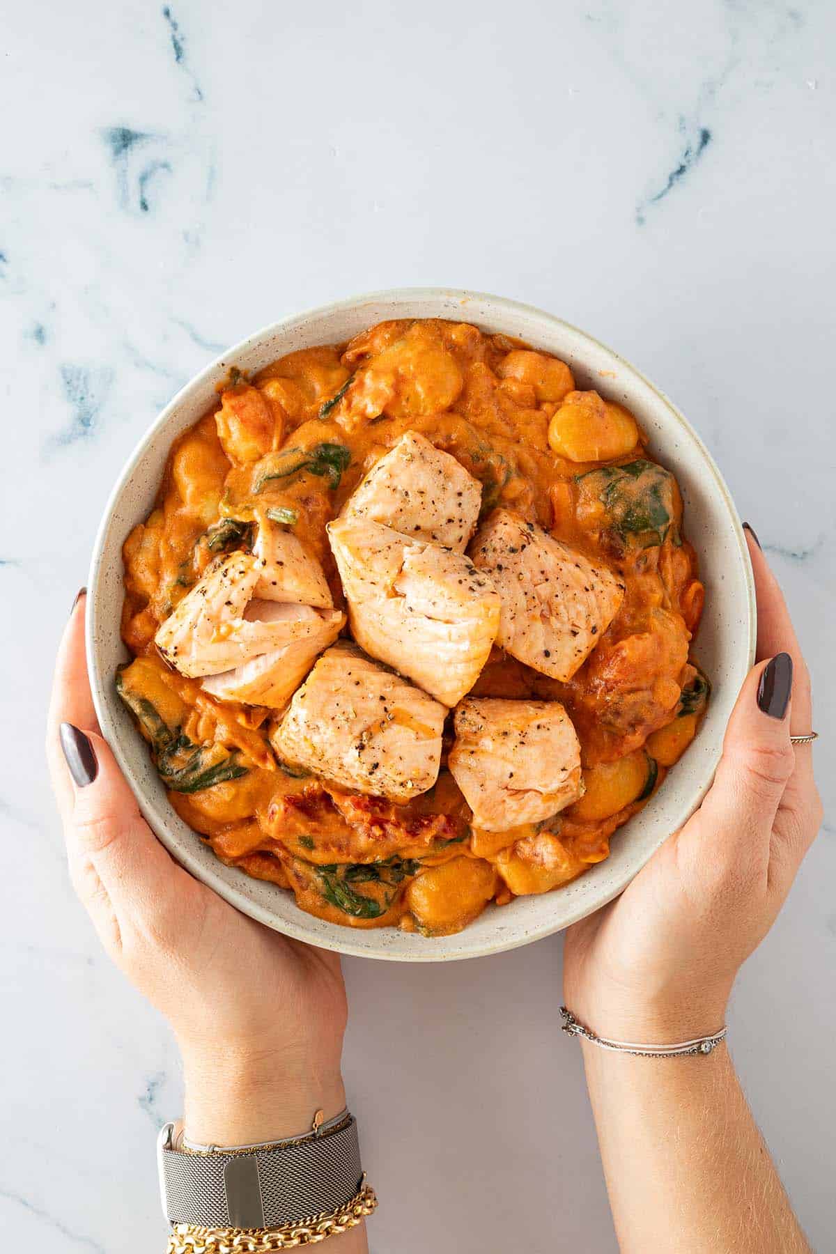 Sch&uuml;ssel mit Gnocchi in cremiger Tomaten-Sahne-Sauce und gebratenen Lachsw&uuml;rfeln, von zwei H&auml;nden gehalten.