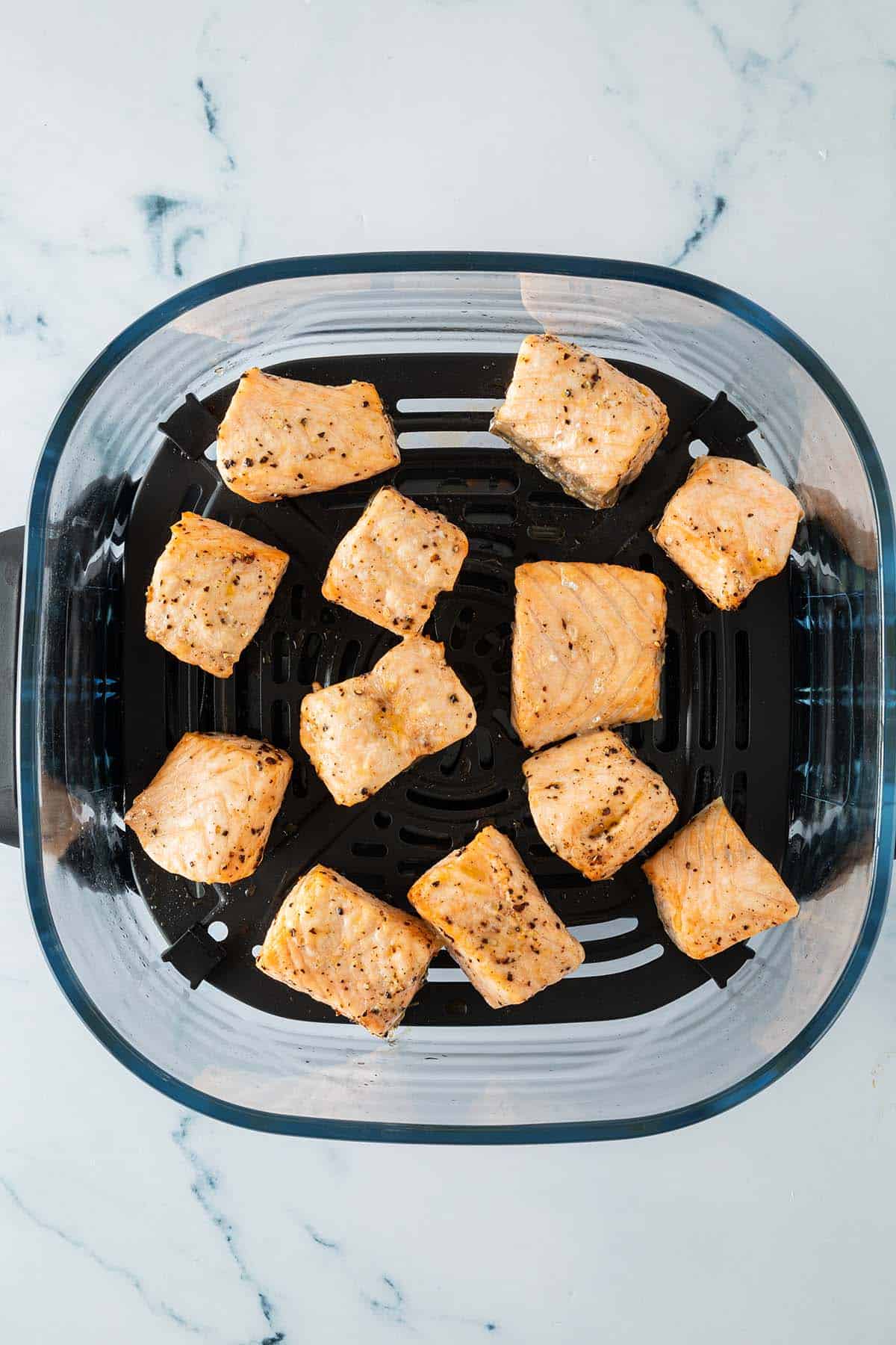 Gegarte Lachsw&uuml;rfel gleichm&auml;&szlig;ig verteilt im Airfryer-Korb.