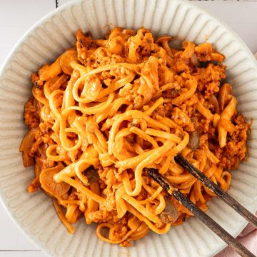 Cremige Gochujang-Nudeln mit gebratenem Tempeh und Pilzen in einer Sch&uuml;ssel, serviert mit Essst&auml;bchen.