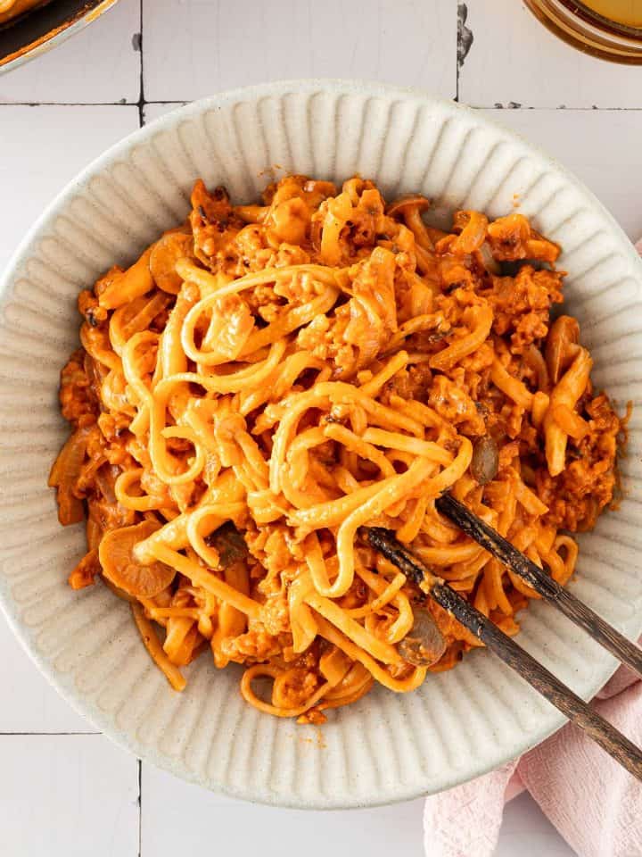 Cremige Gochujang-Nudeln mit gebratenem Tempeh und Pilzen in einer Schüssel, serviert mit Essstäbchen.