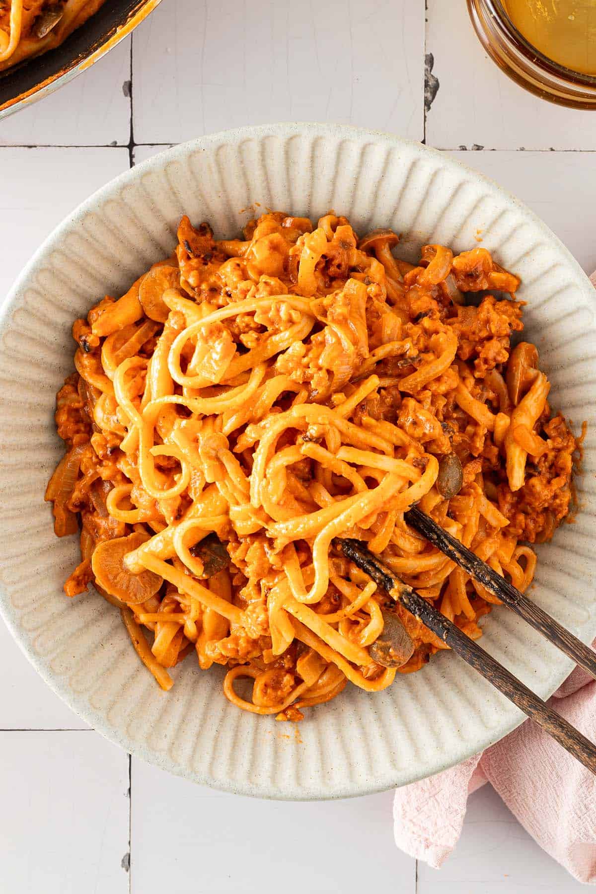 Cremige Gochujang-Nudeln mit gebratenem Tempeh und Pilzen in einer Sch&uuml;ssel, serviert mit Essst&auml;bchen.