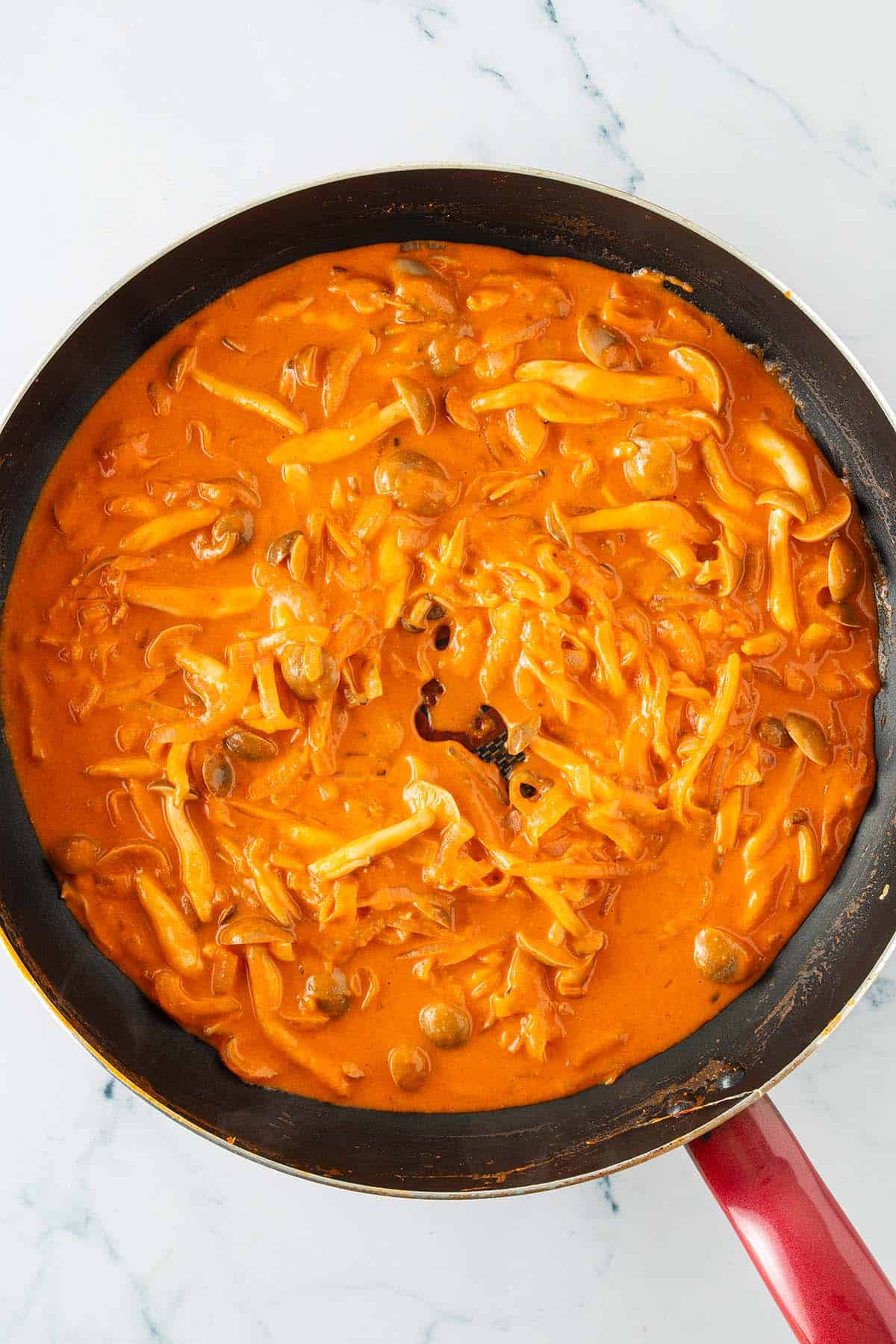 Cremige Gochujang-Sauce mit Pilzen und Zwiebeln k&ouml;chelt in einer Pfanne.