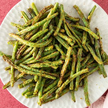 Ein Teller mit im Airfryer gegarte grüne Bohnen auf einem roten Untergrund.