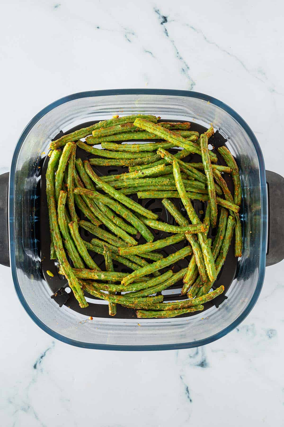 Fertig gegarte grüne Bohnen in einem Glas Airfryer-Korb.