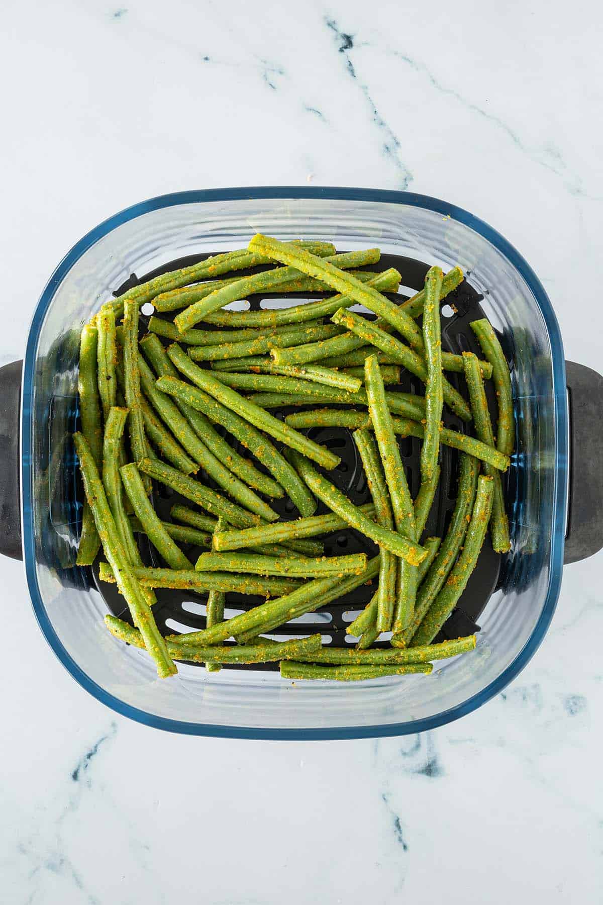 Mit Hefeflocken marinierte grüne Bohnen in einem Airfryer-Korb.