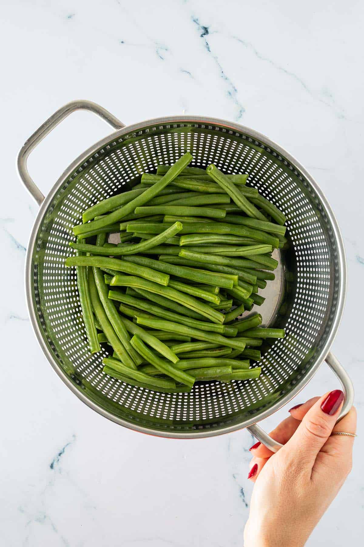 Gewaschene und getrimmte grüne Bohnen in einem Seiher, der von einer Hand gehalten wird.