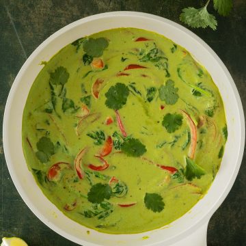 Cremiges gr&uuml;nes Thai Curry in einer Pfanne mit Gem&uuml;se, serviert auf einem dunkelgr&uuml;nen Untergrund.