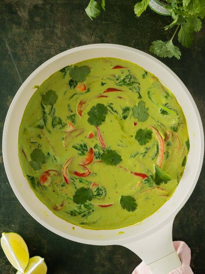 Cremiges grünes Thai Curry in einer Pfanne mit Gemüse, serviert auf einem dunkelgrünen Untergrund.