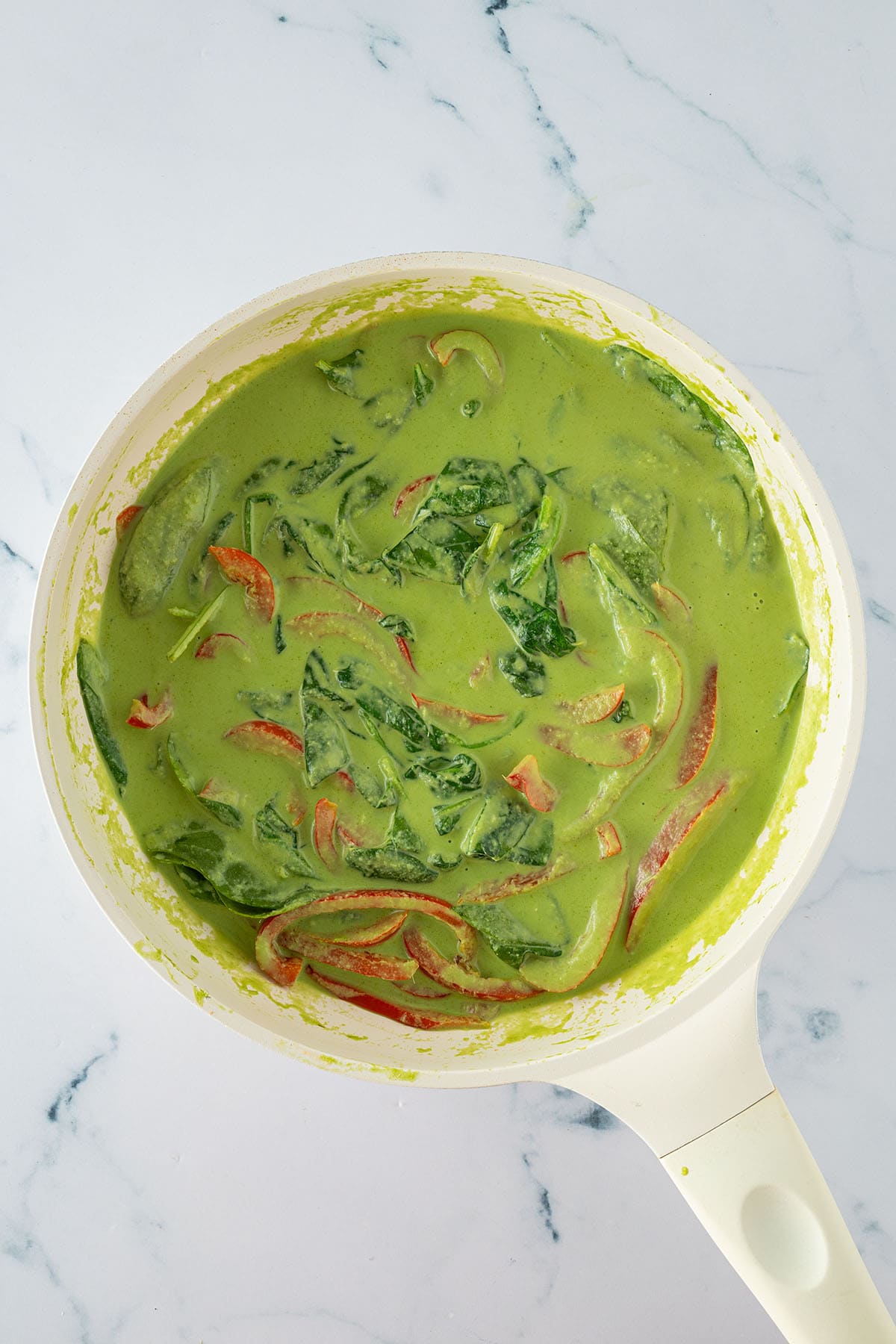 Gr&uuml;nes Thai Curry in einer Pfanne mit Spinat und roten Paprikastreifen.