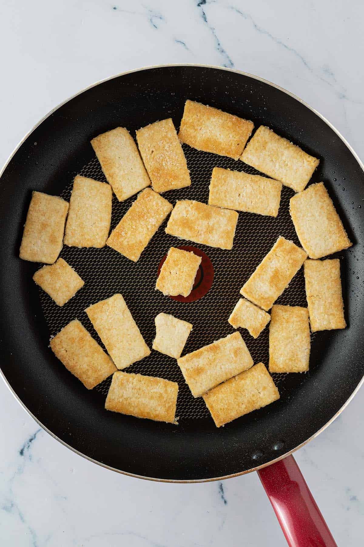 Knusprig, goldbraun angebratene Tofu-Scheiben in einer Pfanne.