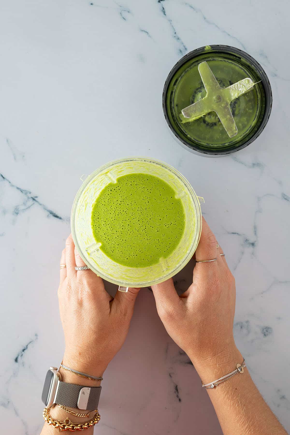 Zwei H&auml;nde halten einen Mixer mit einer gr&uuml;nen Thai Curry Sauce.