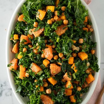 Winterlicher Grünkohlssalat mit Orange, Kürbis und Kichererbsen auf einem ovalen Teller.