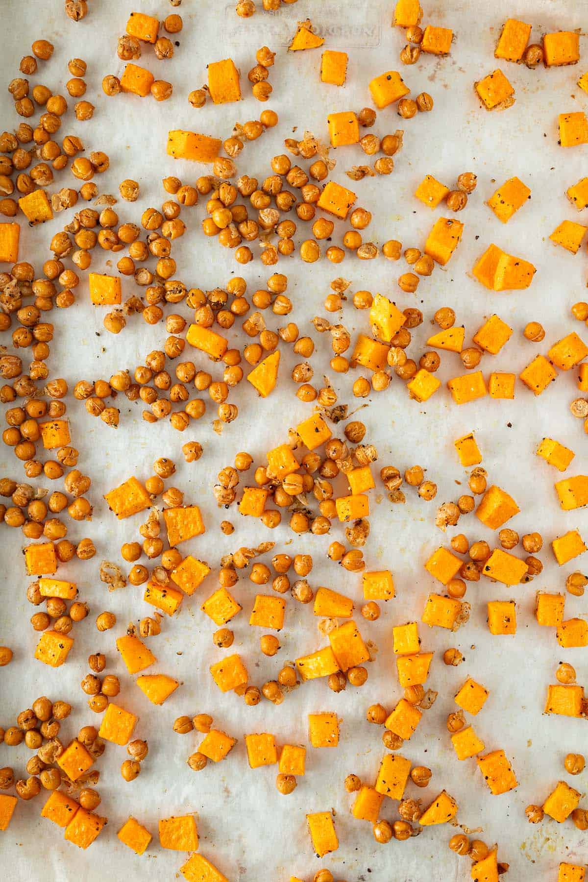 Geröstete Kichererbsen und Kürbiswürfel auf einem Blech mit Backpapier.