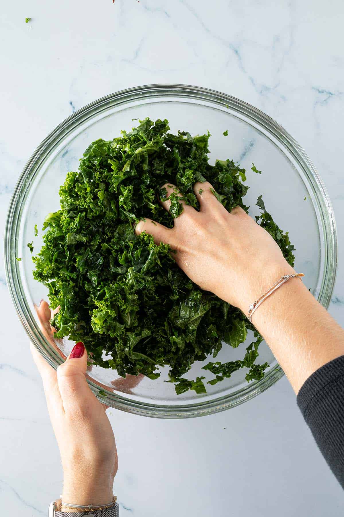 Eine Hand massiert Grünkohlblätter in einer großen Schüssel.
