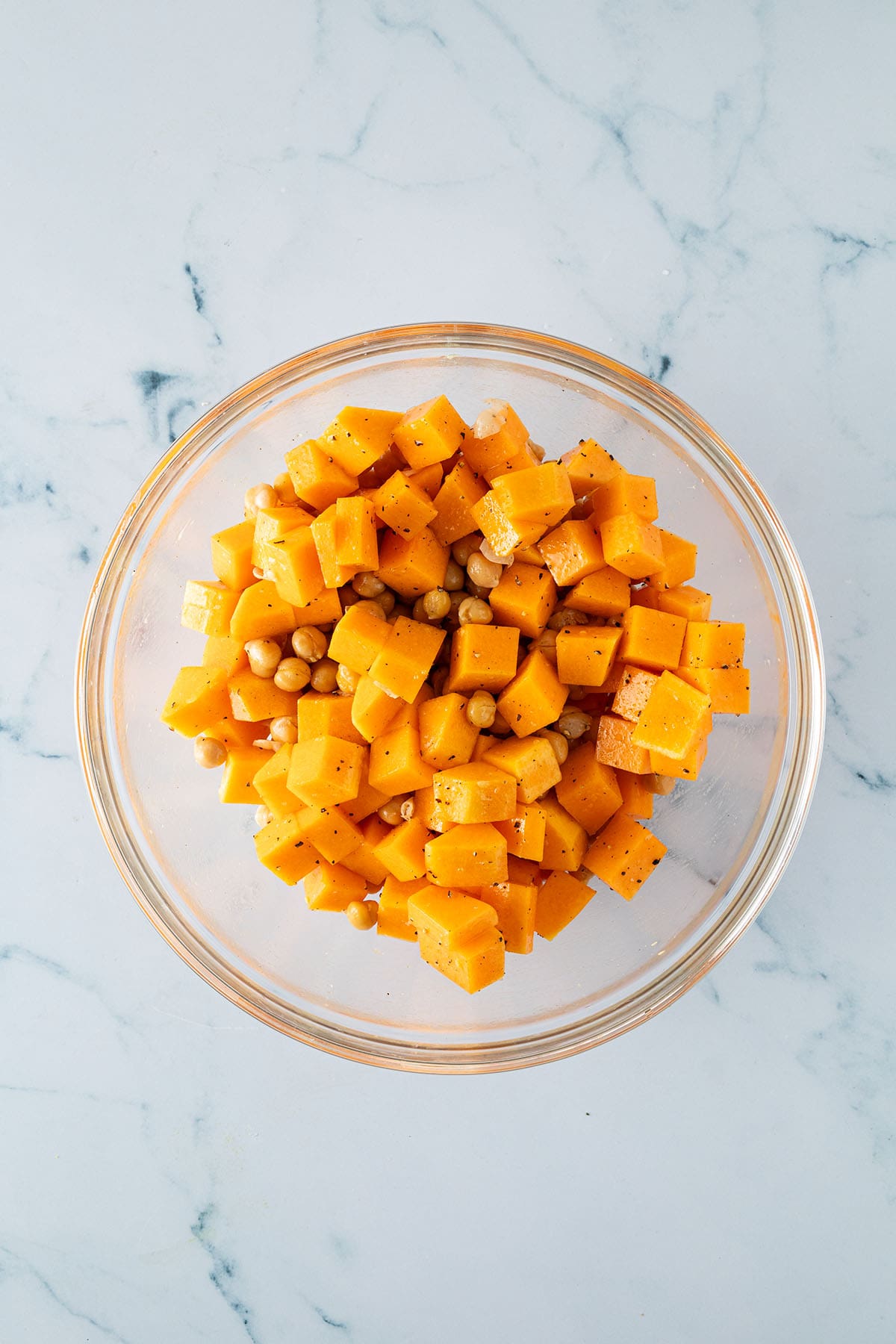 Kürbiswürfel und Kichererbsen in einer Schüssel mit Öl und Gewürzen vermischt.