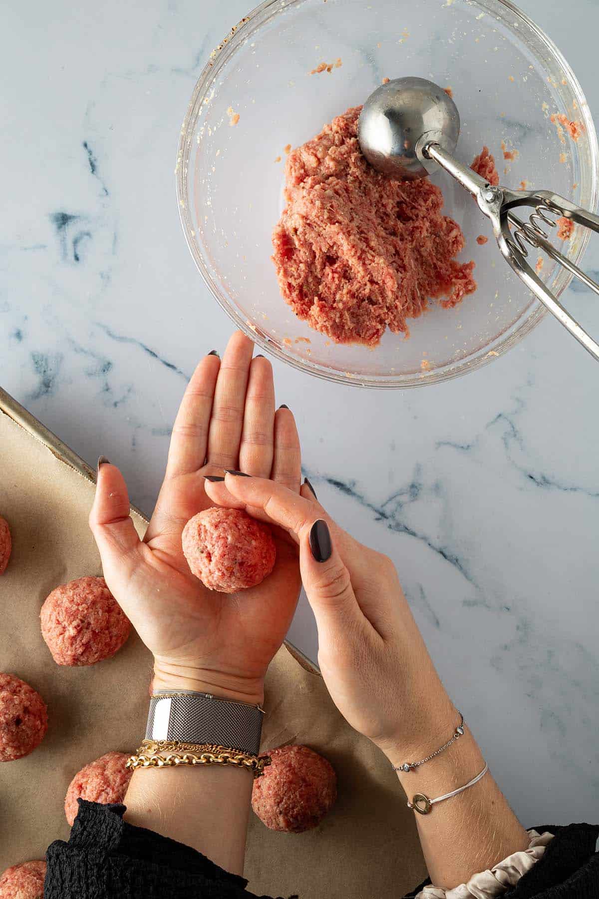 Zwei H&auml;nde formen aus der Hackfleischmasse ein Hackb&auml;llchen, im Bildrand ein Blech mit rohen Hackb&auml;llchen.