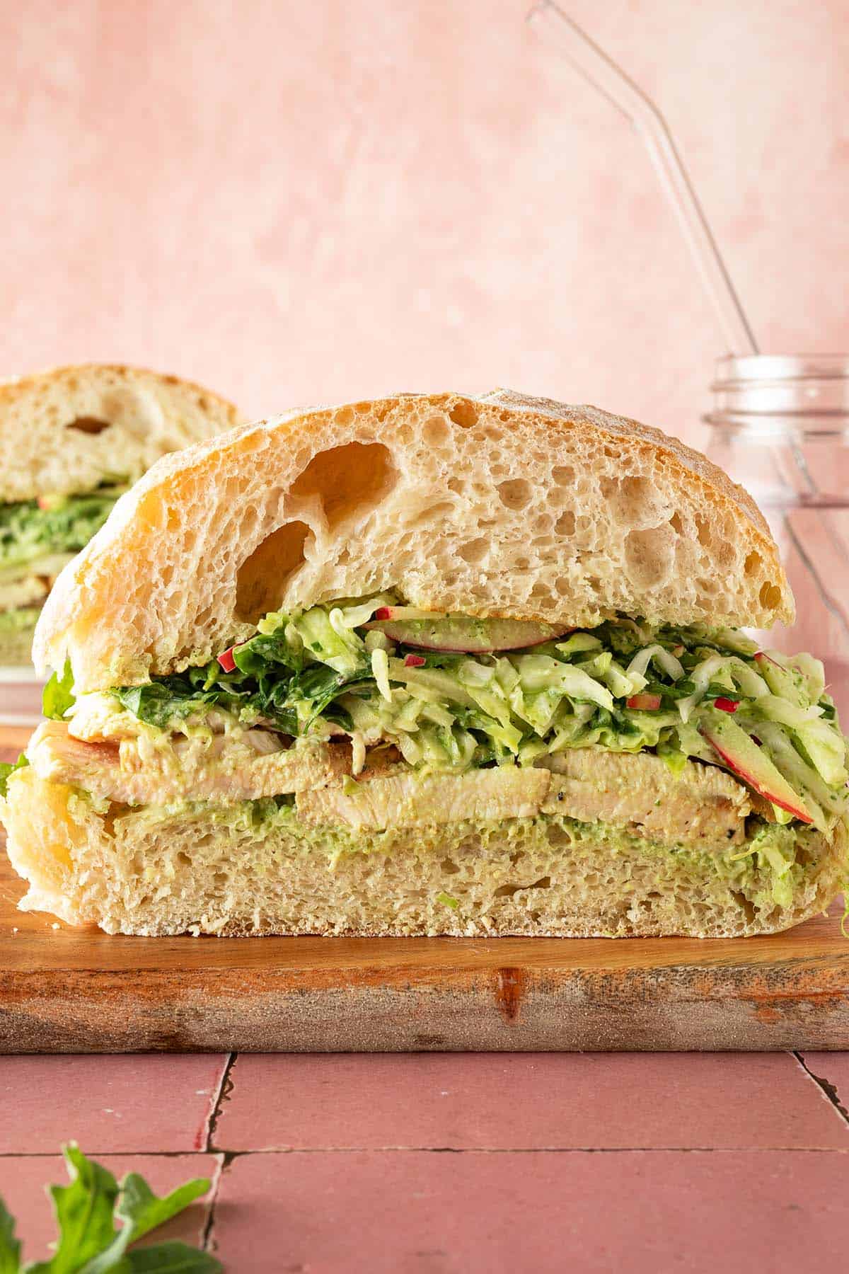 Aufgeschnittenes Ciabatta-Sandwich mit peruanischem H&auml;hnchen, Wei&szlig;kohl-Apfelsalat und cremiger gr&uuml;ner Sauce auf einem Holzbrett.