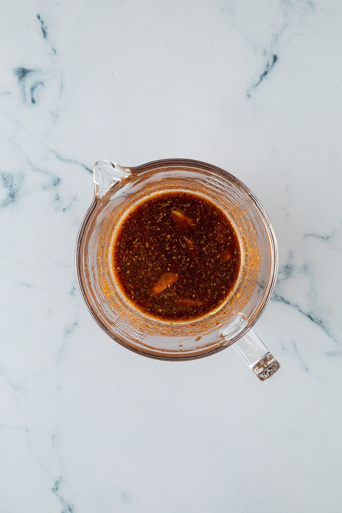 Dunkle Marinade mit Gew&uuml;rzen in einem Messbecher.