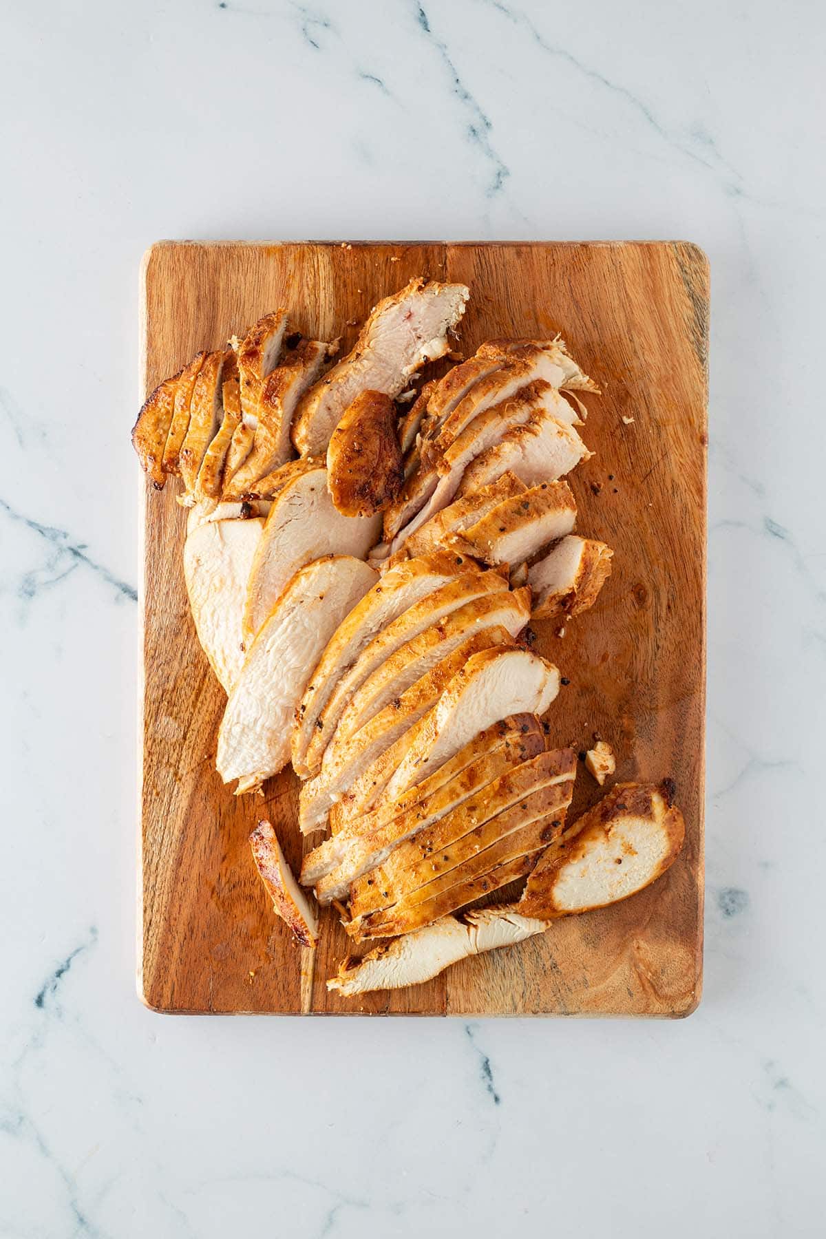 In Scheiben geschnittene, gebratene H&auml;hnchenbrust auf einem Holzbrett.